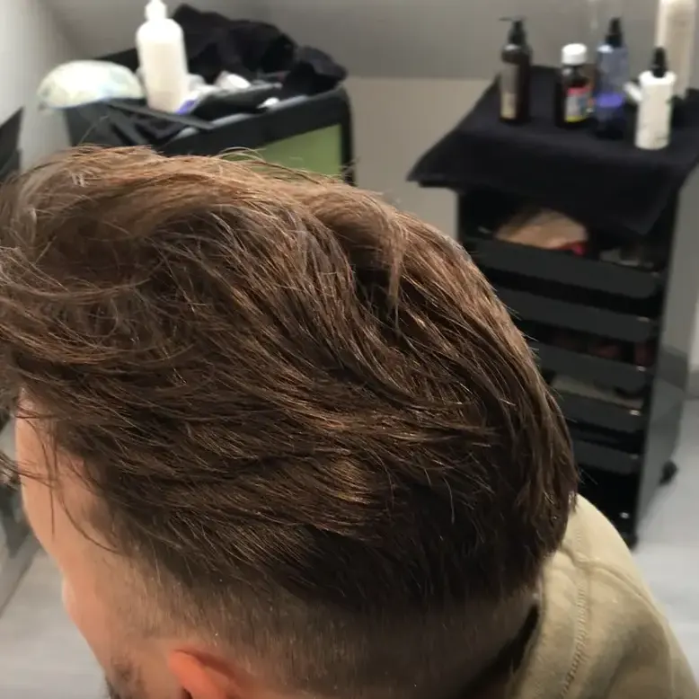 Le même client après, vu de dessus : cheveux châtains coiffés en arrière, dégradé sur les côtés
